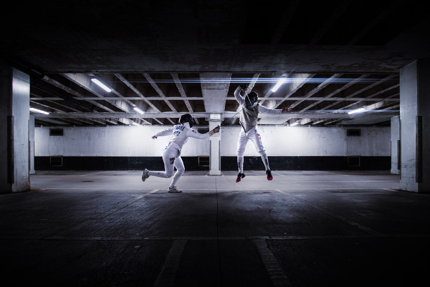 Two GBR fencers duelling under the lights of a concrete garage